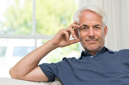 Retired mature man sitting on couch and looking at camera.